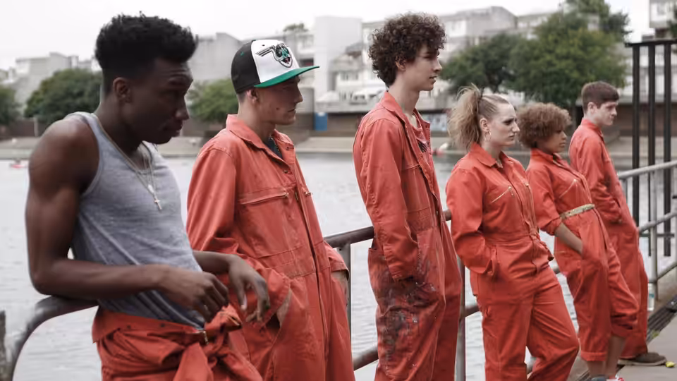 group in red jumpsuits standing by a railing next to a river