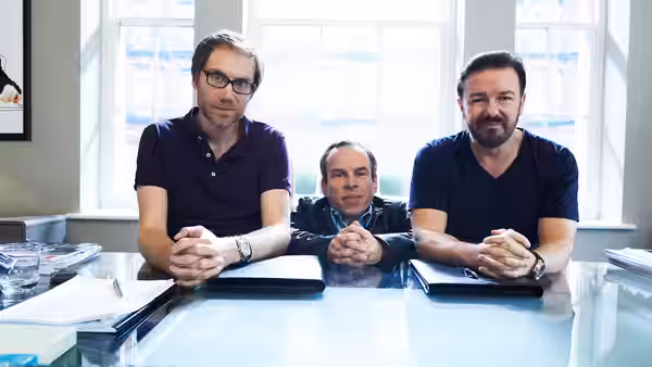 Stephen Merchant (Stephen Merchant), Warwick Davis (Warwick Davis) and Ricky Gervais (Ricky Gervais) seated at a glass desk