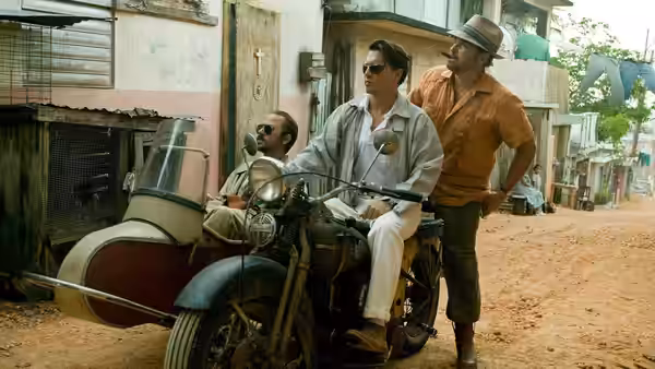 Paul Kemp (Johnny Depp) rides a motorcycle with a sidecar as two men accompany him
