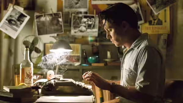 Paul Kemp (Johnny Depp) types at a desk beside a smoking bottle in a cluttered office