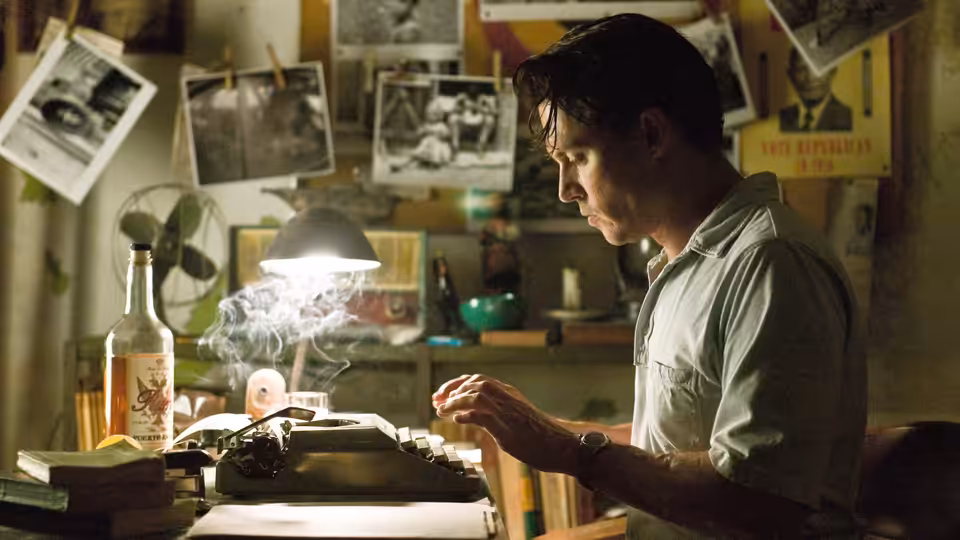 Paul Kemp (Johnny Depp) types at a desk beside a smoking bottle in a cluttered office