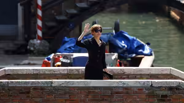Elise Clifton-Ward (Angelina Jolie), wearing sunglasses, waves from a Venetian canal-side walkway