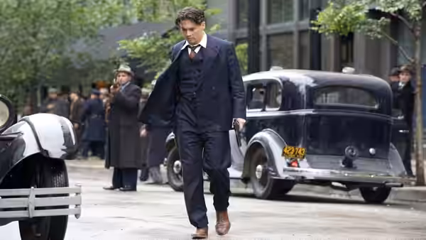 Melvin Purvis (Christian Bale) walks past parked cars on a city street