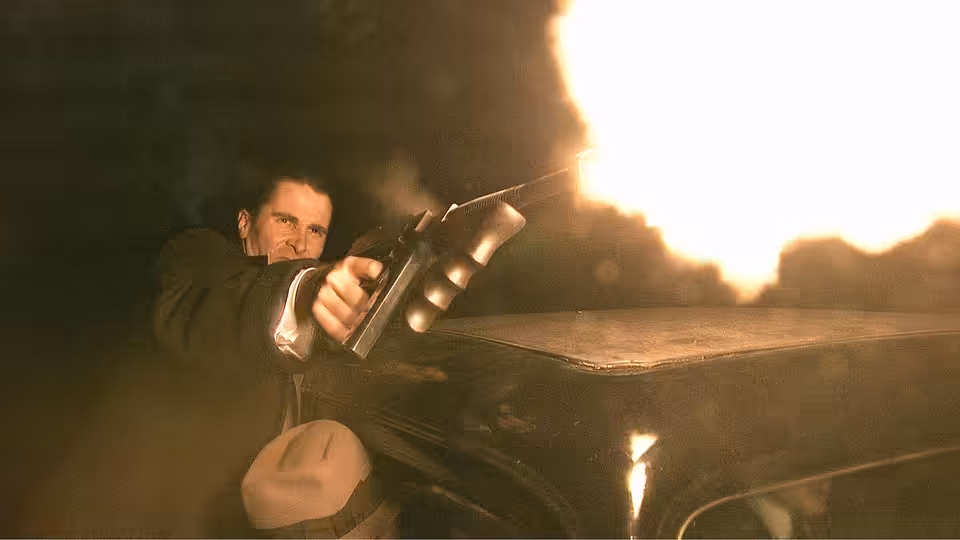 John Dillinger (Johnny Depp) aims a gun from beside a car as flames blaze behind him