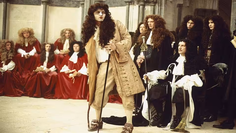 Rochester (Johnny Depp) stands before the seated king and courtiers in a royal chamber