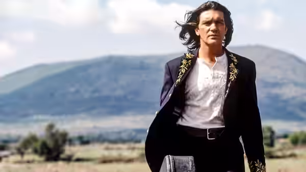 El Mariachi (Antonio Banderas) walks across open countryside carrying a guitar case