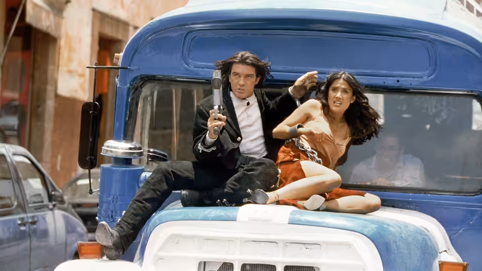 CIA Agent Jeffrey Sands (Johnny Depp) and Carolina (Salma Hayek) crouch atop a vehicle as Sands raises a gun