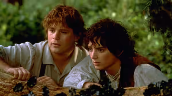 Merry (Dominic Monaghan) and Pippin (Billy Boyd) peering over a log in the woods