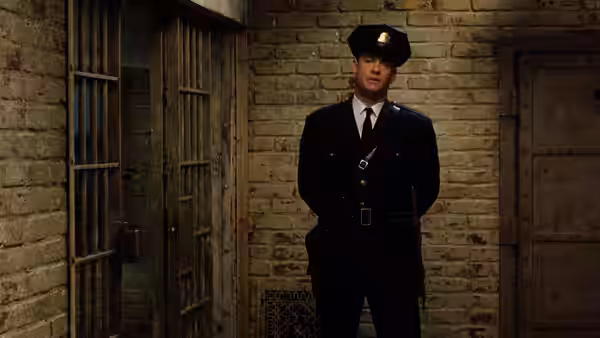 A prison guard stands with hands behind his back in a brick corridor
