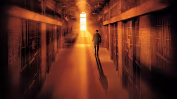 A man walks down a long prison corridor toward bright light