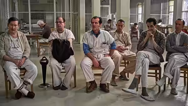 Patients in white uniforms seated in a row inside a large hall