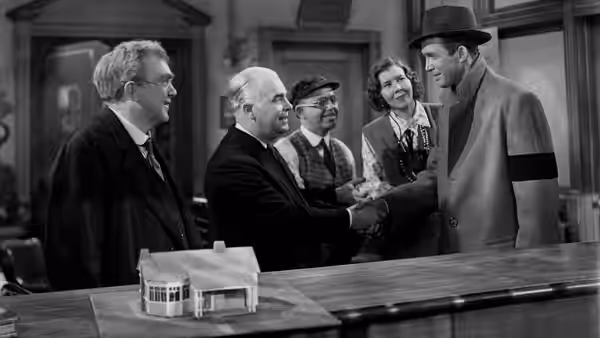 George Bailey (James Stewart) shakes hands during a meeting in an office