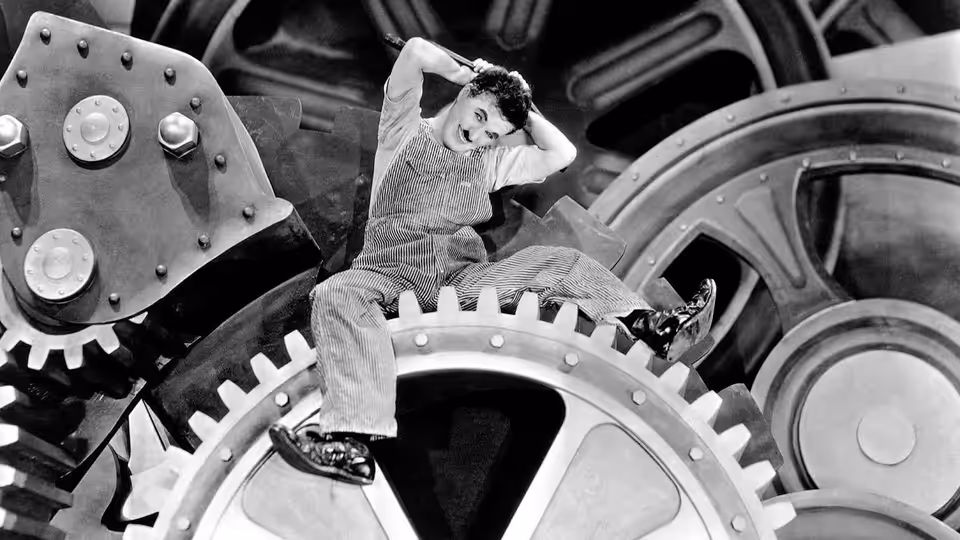 The Tramp (Charlie Chaplin) lounging atop a giant factory gear