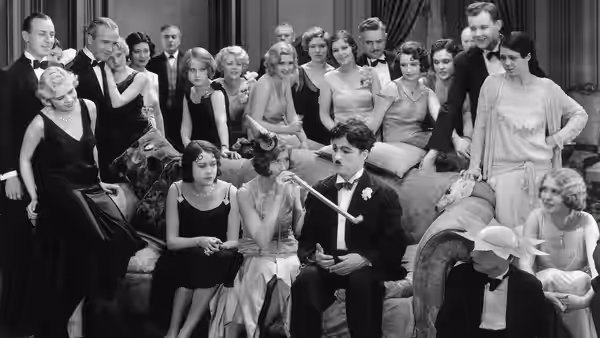 The Tramp (Charlie Chaplin) sits among formally dressed guests at a party