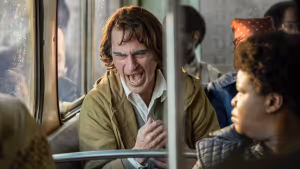 Arthur Fleck (Joaquin Phoenix) laughing on a bus next to a young boy