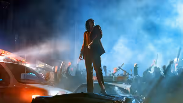 Arthur Fleck (Joaquin Phoenix) standing on a car amid a nighttime crowd