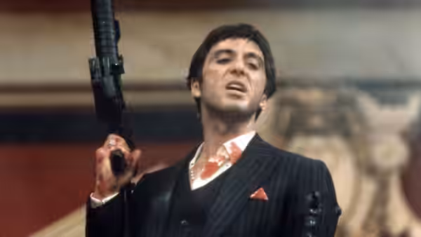 Tony Montana (Al Pacino) raising a machine gun with mouth open in a suit