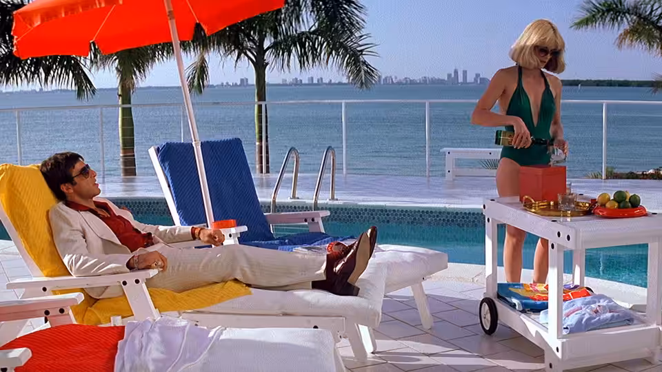 Tony Montana (Al Pacino) reclining poolside as Elvira (Michelle Pfeiffer) prepares drinks