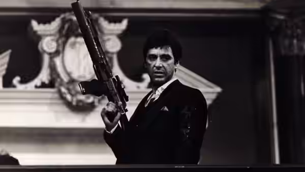Tony Montana (Al Pacino) holding a machine gun while standing in formal hall