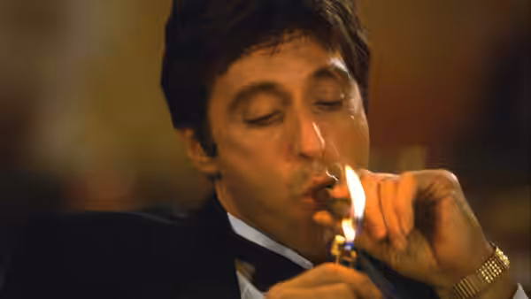 Tony Montana (Al Pacino) lighting a cigar using a gold lighter up close