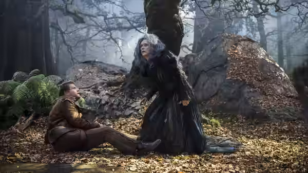 The Witch (Meryl Streep) stands over the seated Baker (James Corden) in the woods