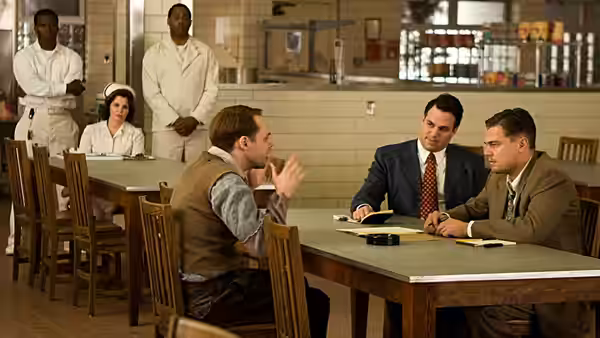 Teddy Daniels (Leonardo DiCaprio) sits at a table with two men in the mess hall