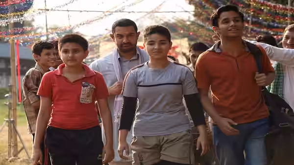 Mahavir Singh Phogat walking with boys under colorful outdoor decorations