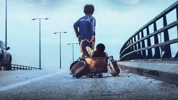 A boy stands on a cart on a highway bridge while another sits inside