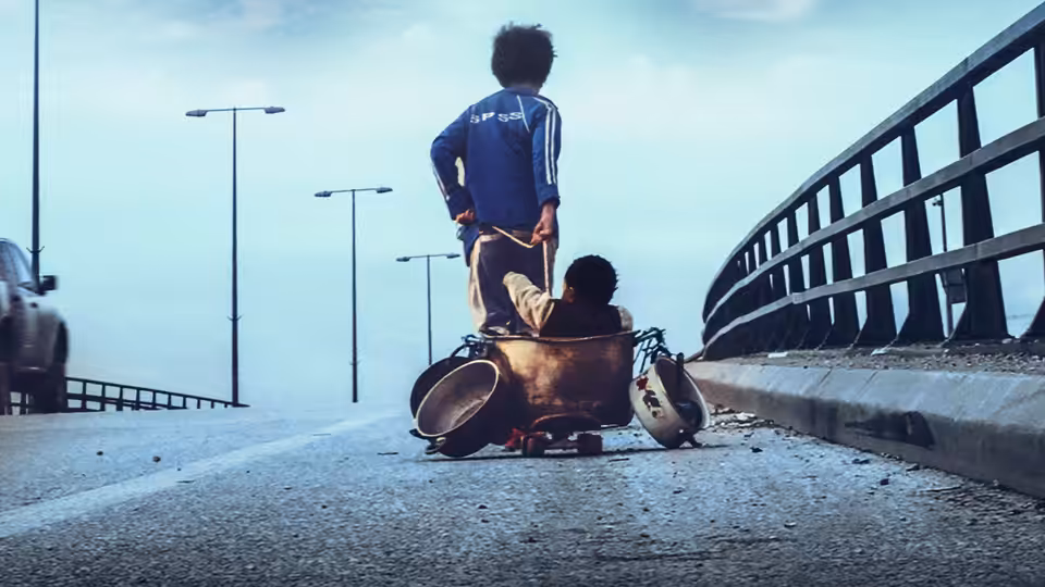A boy stands on a cart on a highway bridge while another sits inside