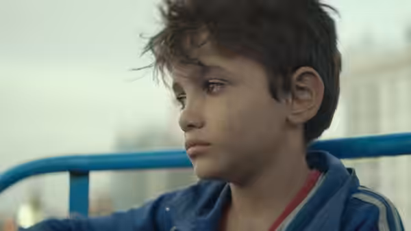 A boy with curly hair looks to the side with a serious expression