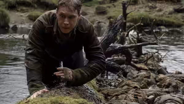 A soldier crawls from a river onto a moss-covered log