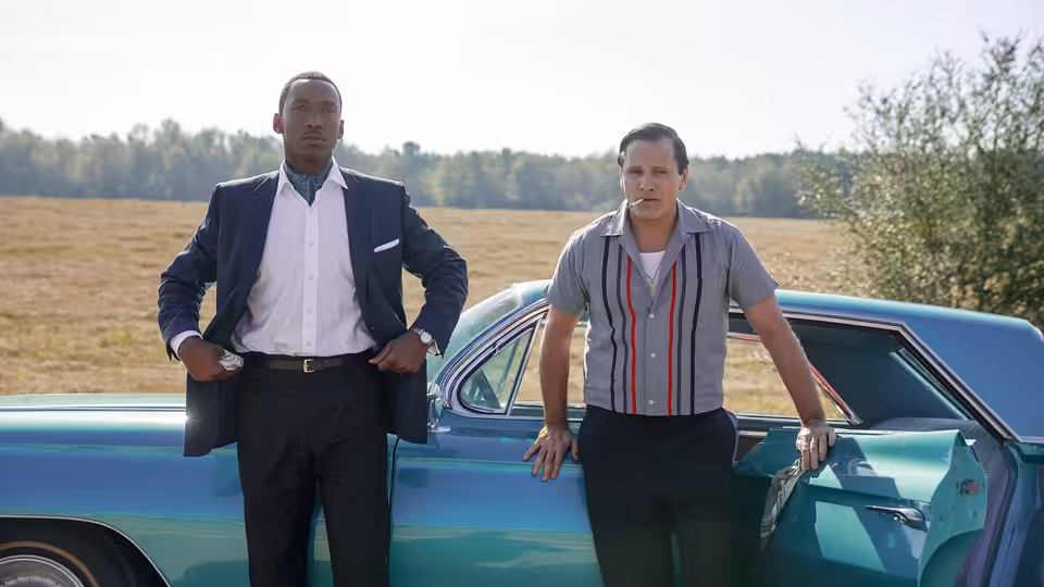 Dr. Don Shirley (Mahershala Ali) and Tony Lip (Viggo Mortensen) leaning against a turquoise car in a field