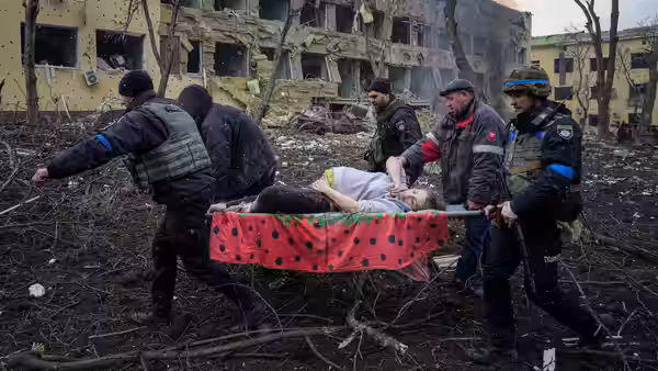 Rescue workers carrying an injured person on a stretcher through rubble near a damaged building