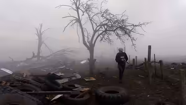 Person walking through a foggy devastated area with bare trees and scattered tires