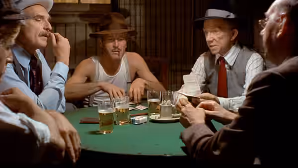Men play cards around green table with beers and cash