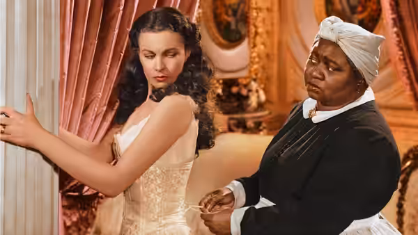 Scarlett O'Hara (Vivien Leigh) stands as Mammy (Hattie McDaniel) adjusts her gown