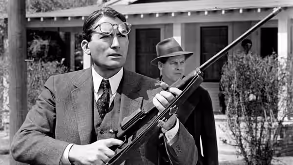 Atticus Finch (Gregory Peck) holding a rifle outside a house
