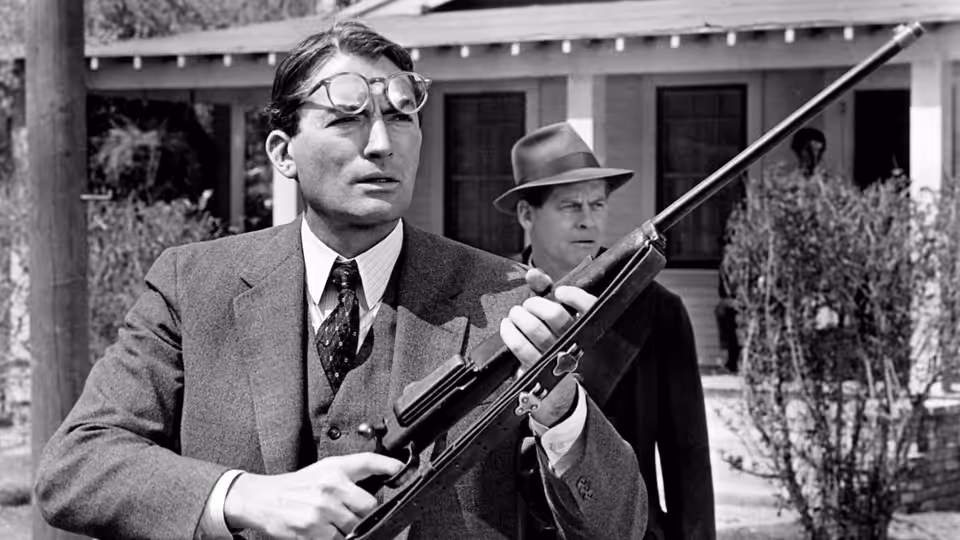 Atticus Finch (Gregory Peck) holding a rifle outside a house