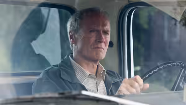 Walt Kowalski (Clint Eastwood) driving a pickup truck down the road