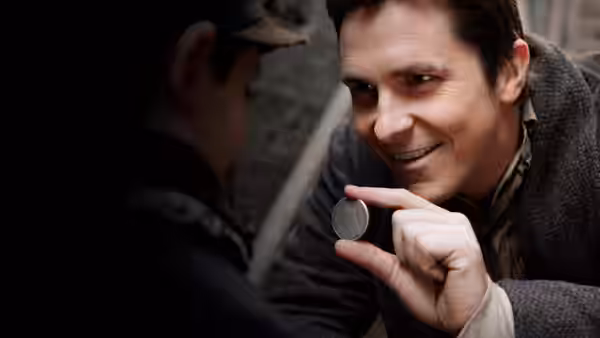 Alfred Borden (Christian Bale) smiling as he holds up a small coin