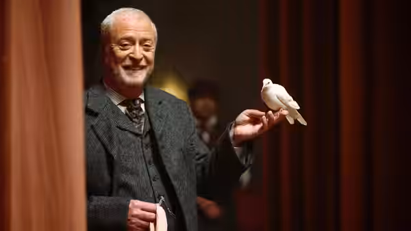 Cutter (Michael Caine) holding a white dove on his fingertip near a curtain