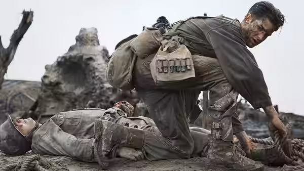 A bloodied soldier kneeling over a fallen comrade on muddy ground