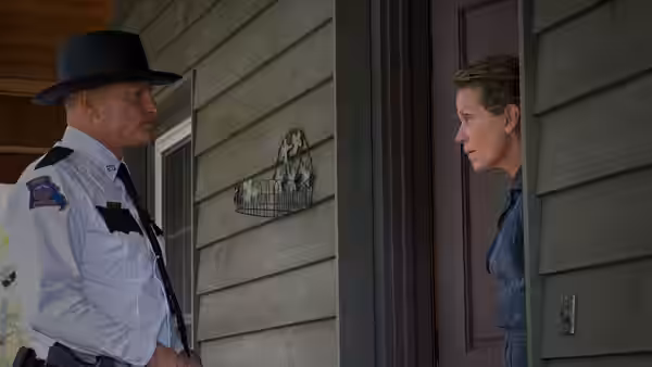 A sheriff speaks with Mildred (Frances McDormand) at a house doorway