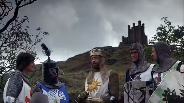 King Arthur and knights in armor stand on a hill before a castle