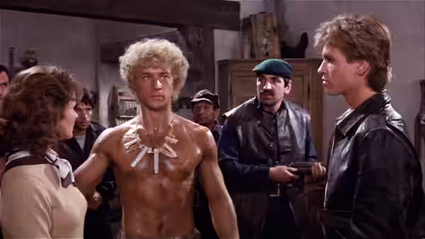 Nick Rivers (Val Kilmer) faces a shirtless man as armed men watch in a crowded room