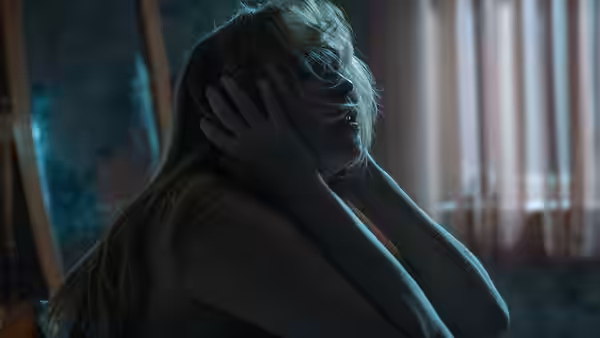 Grace (Jennifer Lawrence) clutching her head while seated in a room