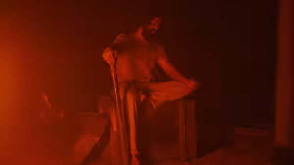 Rocky (Yash) sitting on a wooden crate holding a long stick