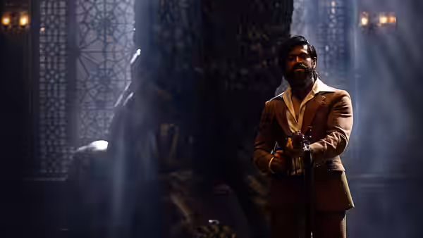 Rocky (Yash) holding a gun while standing before a large statue