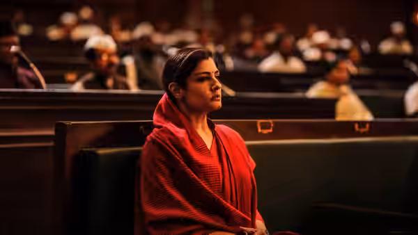Ramika Sen (Raveena Tandon) seated in a wooden pew inside a hall
