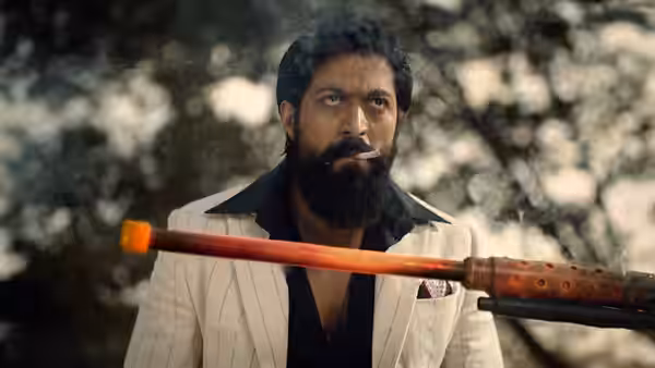 Rocky (Yash) smoking a cigar with a rifle in the foreground